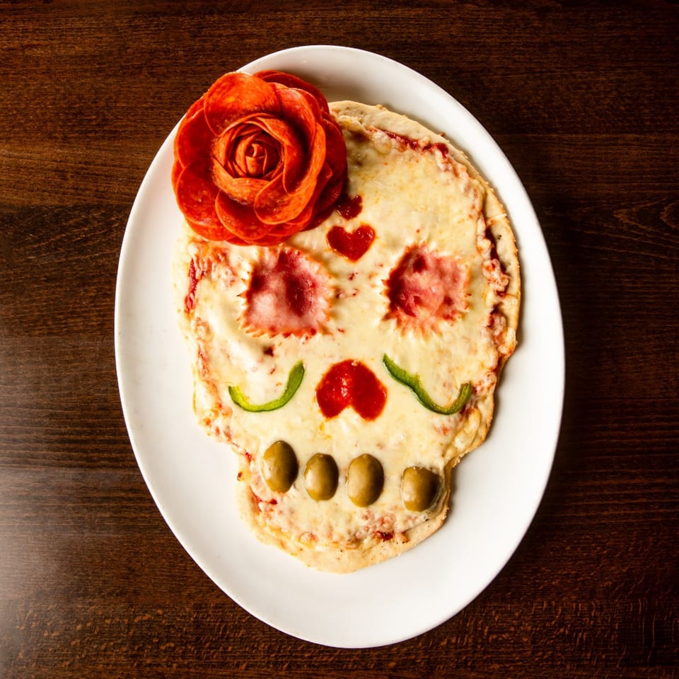 Gelsosomo's Pizzeria's skull-shaped pizza with pepperoni rose, olive teeth, and pepper mustache on a white plate.
