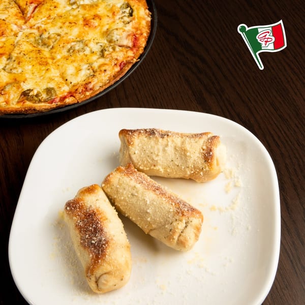 Three Gelsosomo's Pizzeria garlic knots on a white plate with a pizza in the background.