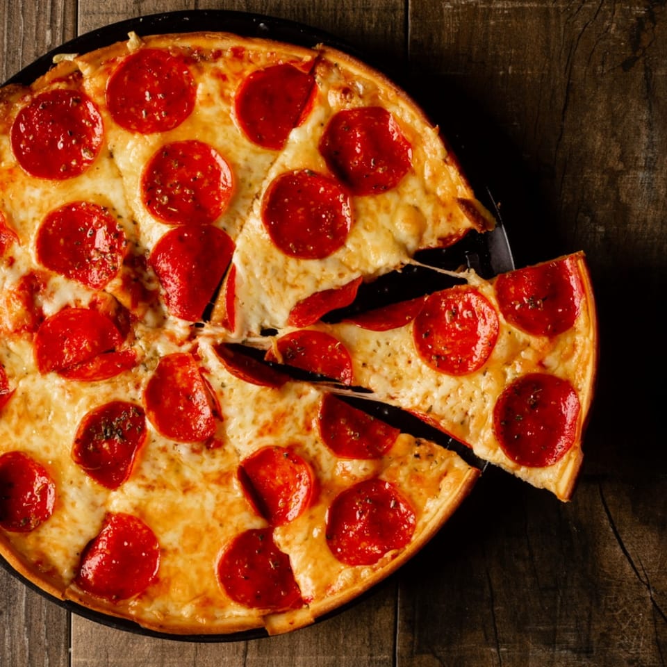 A Gelsosomo's Pizzeria pepperoni pizza with a slice being pulled away, on a wooden table.